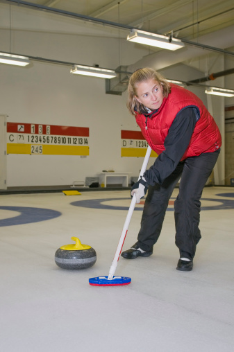 Candid of a curler sweeping during a game. Rock is on ice near broom she is holding. Curling is an official . winter sport.