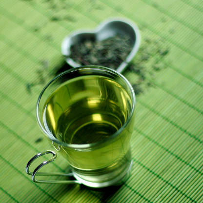 Transparent cup of green tea on green background, selective focus.