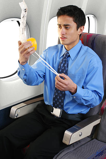 Young male looking concerned at the oxygen mask Passenger on a commercial airliner putting on an oxygen mask. oxygen mask plane stock pictures, royalty-free photos & images