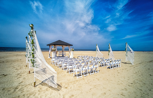 Wedding altar and row of white chairs prepared on the beach against a background of beautiful sea and blue sky. Destination wedding and celebration in a tropical country concept.