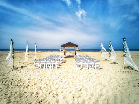 Wedding altar and row of white chairs prepared on the beach against a background of beautiful sea and blue sky. Destination wedding and celebration in a tropical country concept.