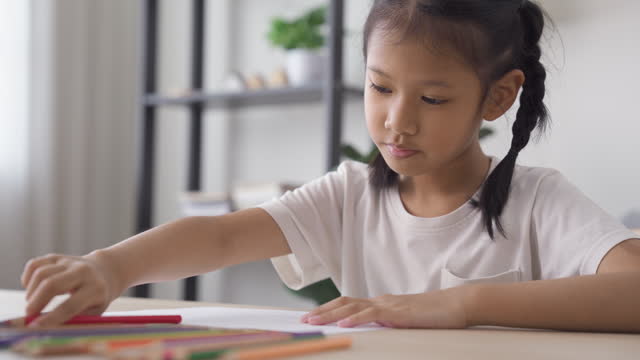 A girl enjoys coloring and drawing on a paper at home. Kid with paint arts