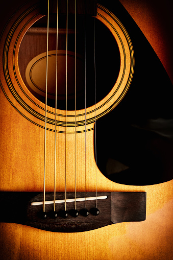 Closeup detailed view of acoustic guitar soundboard, bridge and strings. Musical instruments and music theme. Yellow glowing color