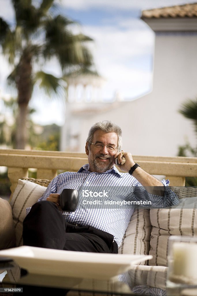 On the Phone Mature man smiling on the phone on balcony with blue sky and palm tree in the background 50-59 Years Stock Photo