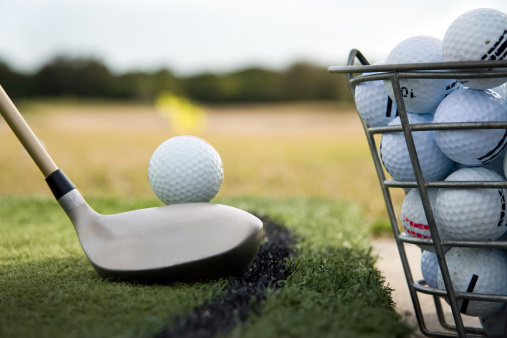 Close up of a golf club preparing to hit a  practice golf ball at a driving range.     