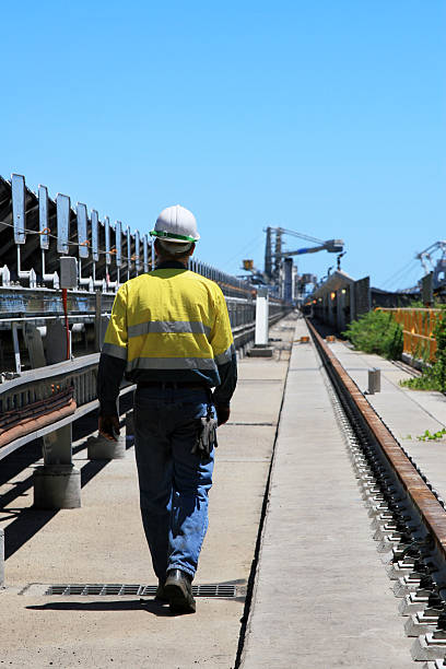 A coal terminal workman walking outdoors Workman in safety uniform walking beside a coal conveyer belt with coal terminal loaders in the background. Click to see more... mining conveyor belt stock pictures, royalty-free photos & images