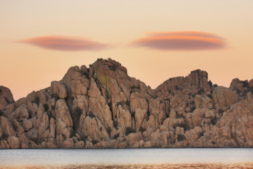 Unusual lenticular clouds appear like flying saucers suspended above wilderness lake in sunset scene just before dark.  Granite Dells, Watson Lake, 2009.