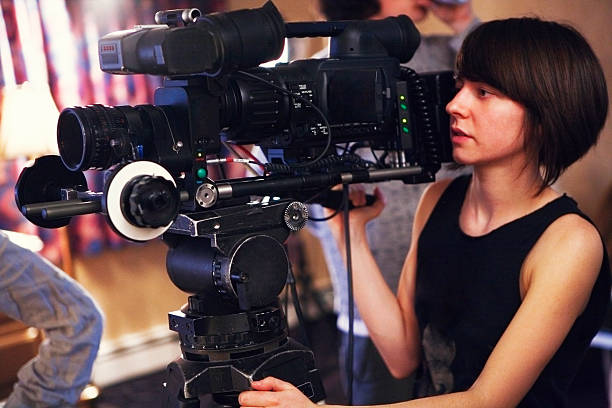 Filming "A young woman operating camera on a video shoot. Camera has a 35mm adaptor on it. Shot on a real set at high iso, some noise, view at 100%.More filmmaking images:" director stock pictures, royalty-free photos & images