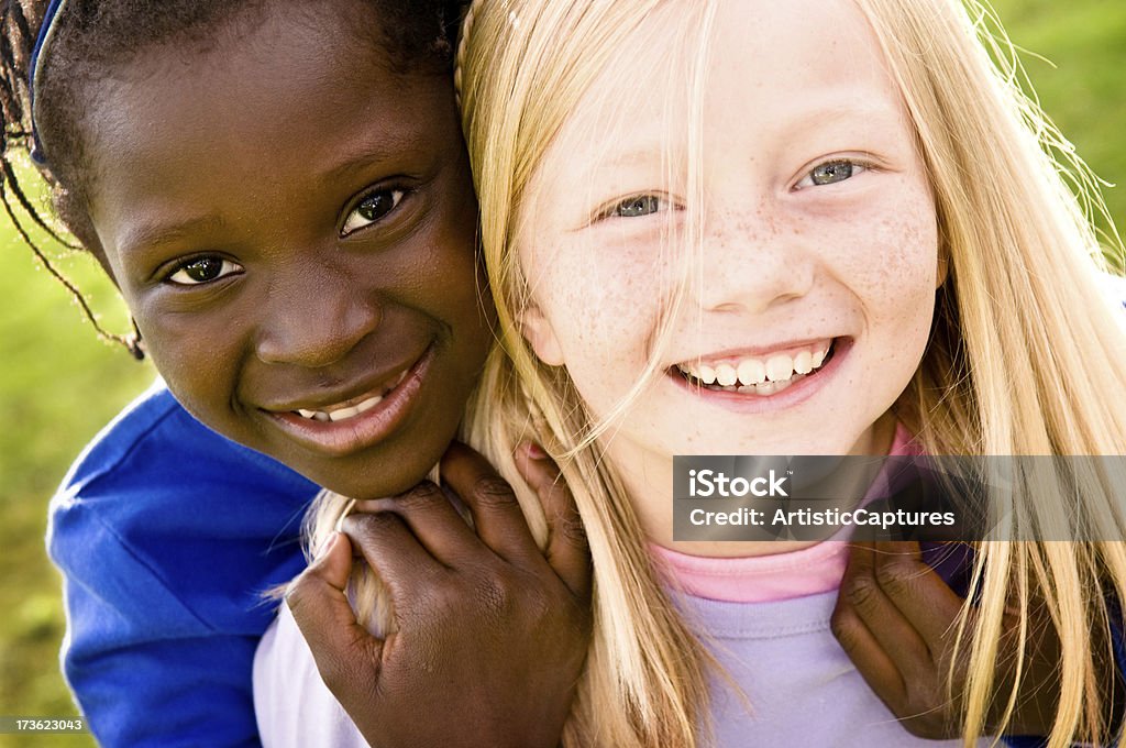 Two Happy Girls Smiling and Playing Together Outside Color photo of two happy girls smiling outside. They are sisters by adoption. Embracing Stock Photo