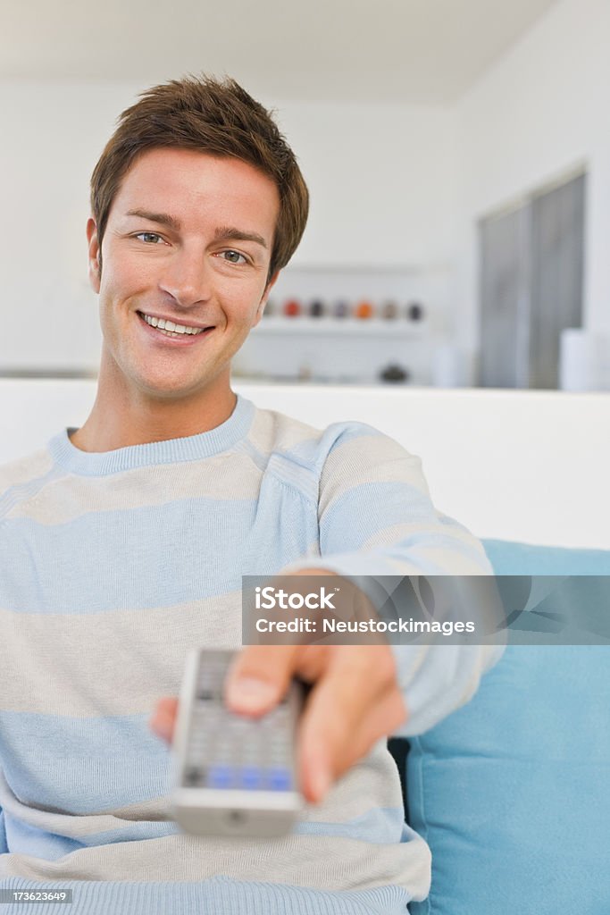 Happy young man holding remote control Portrait of a smiling young man holding remote control 20-24 Years Stock Photo