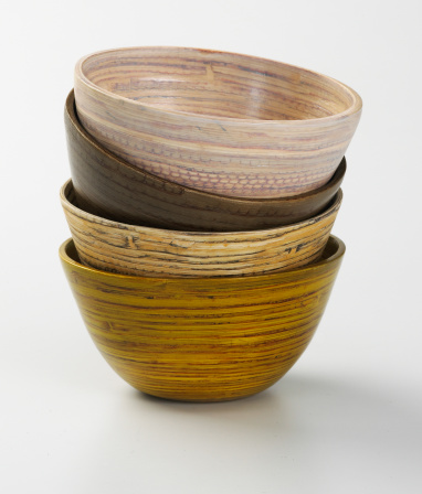 Four stacked bamboo bowls photographed in a still life setting on a white background.