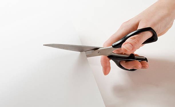 Close up of hand holding scissors and cutting through paper Cutting a piece of paper with a black scissor. White background. scissors stock pictures, royalty-free photos & images