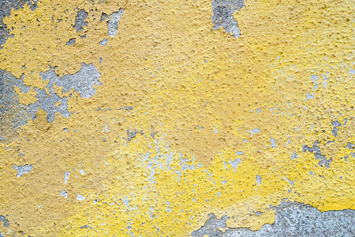 Flaking yellow paint on the stucco exterior wall of an old house