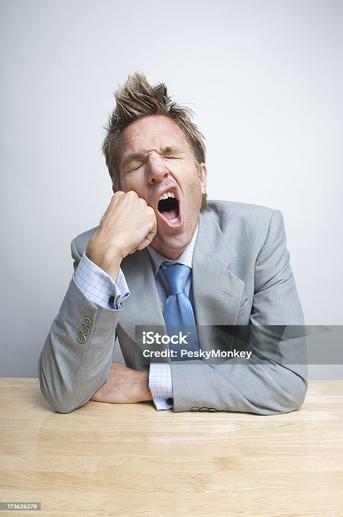 Bored Tired Businessman Office Worker Yawning at His Desk Bored tired businessman office worker sitting at a blond wood desk gives a big yawn Adult Stock Photo