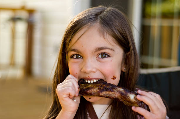 A young girl chowing down on a rib A young girl enjoys her BBQ ribs rib food stock pictures, royalty-free photos & images