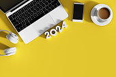 2024 New Year, Empty Screen Smartphone, Wireless headphones, a cup of coffee and  Laptop on Yellow Background.