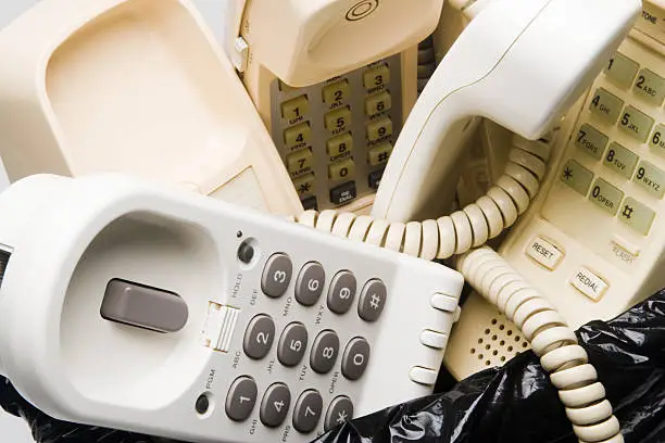 "Close-up of landline telephones in a wastepaper basket, handsets and bases, white and beige, phone cordsOther telephones in waste basket photos"