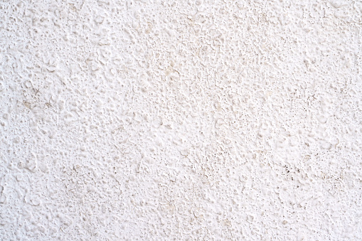The surface of a white painted concrete wall features a grainy, harsh, raw, uneven, and porous texture.