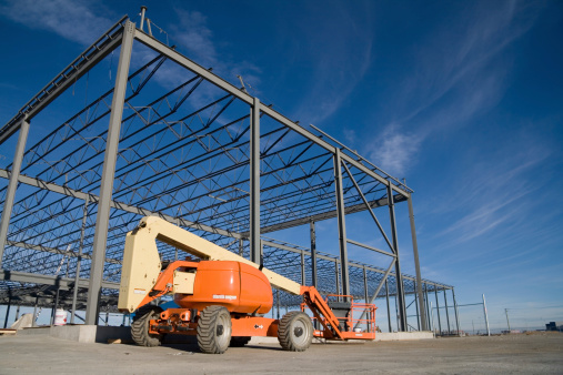 A cherry picker sits next to a newly constructed metal frame building.