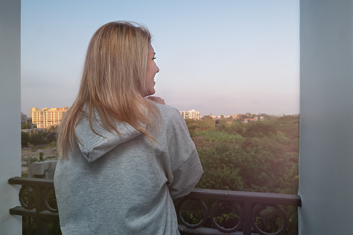 Happy girl stands on the balcony and looks at the sunset