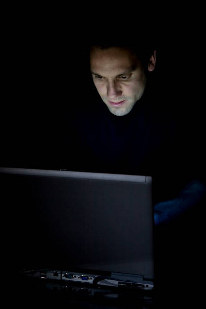 istock A man in the dark using a black laptop looking sneaky 173634586