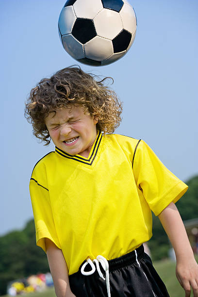 young boy grimaces as he attempts to hit a soccer ball with his head.