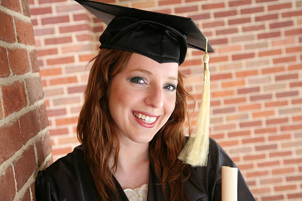 Young beautiful blond female in graduation cap with emotional facial expression on red background. Happy to finish school, college or university High quality photo