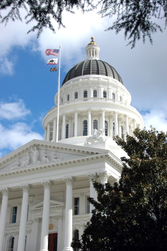 Rotunda and columns of the California State Capitol against blue sky and clouds. Flags blowing in the breeze.