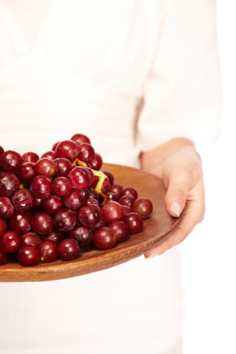 Crop of woman offering a plate full of juicy red grapes on a wooden platter