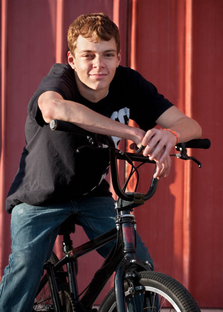 adolescente sonriente en bicicleta al aire libre con fondo de metal roja - bmx cycling sport teenagers only teenager fotografías e imágenes de stock