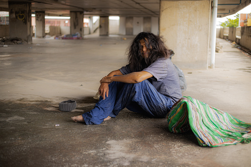 A homeless man sleeps under a ratty blanket on a hard stone sidewalk