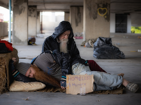 Homeless man with money tin and cardboard sign sitting and begging for money on the street