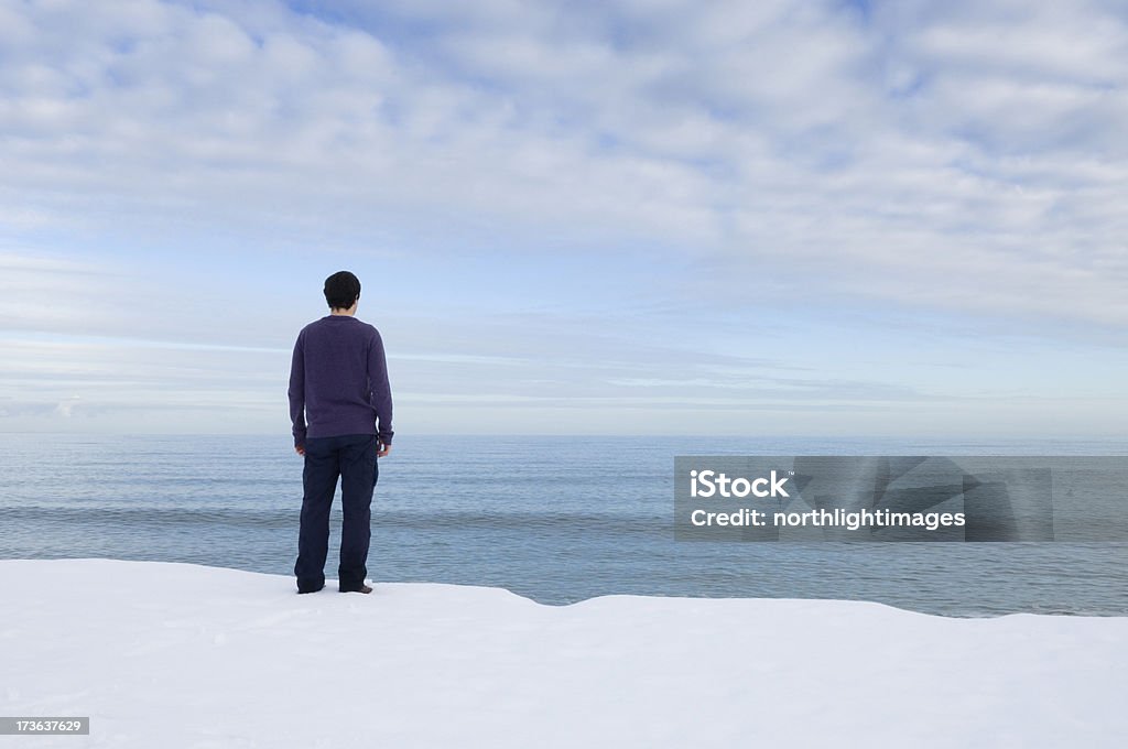 Young man looking out to sea "Young man looking out to sea, at a snow-covered shore. Space for copy." Adult Stock Photo
