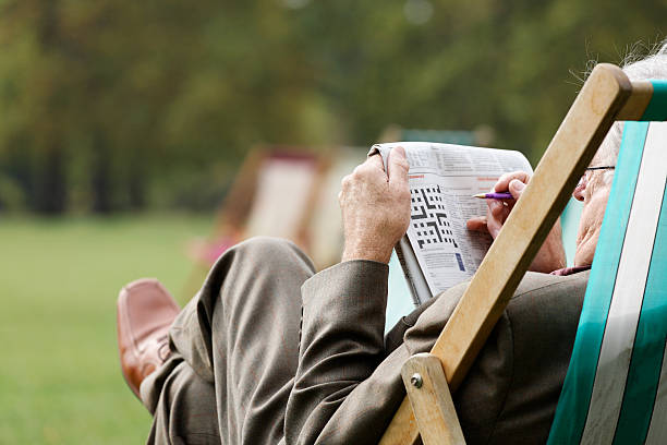 Elderly man sitting in deckchair outside doing crossword A senior gentle man relaxing and doing the crossword crossword stock pictures, royalty-free photos & images