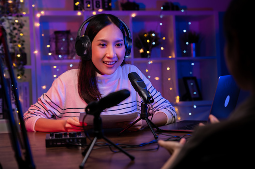 Young Asian woman in green shirts use microphones wear headphones with laptop record podcast interview for radio. Content creator concept.