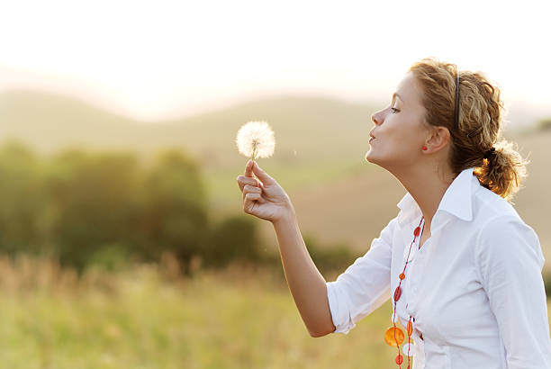 istock Woman blowing a dandelion in a field 173641072