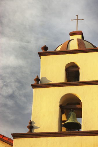 Vintage southwest mission style church belltower with dome in warm sunset lighting as sky clears after storm.