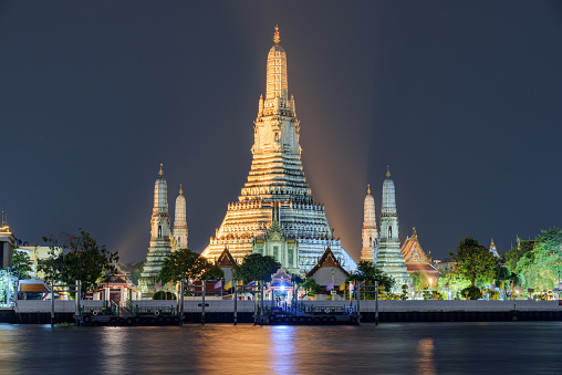 Awesome night view of Wat Arun across the Chao Phraya River in Bangkok, Thailand. The Buddhist temple is a landmark of Bangkok and a popular tourist attraction of Thailand.