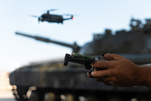 a man with a UAV control panel in his hands, a drone flying above the tank in the background in nature. help of reconnaissance drones in modern warfare.