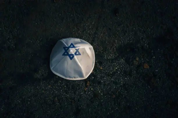 knitted kippah cap in the Israeli flag style on a dark asphalt road background