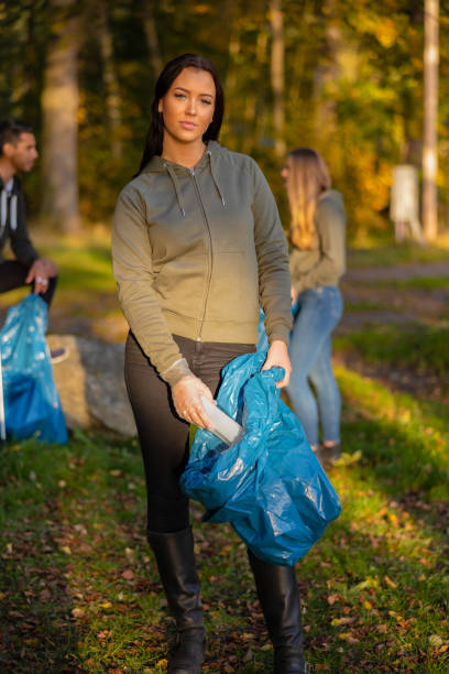 une jeune bénévole devant son équipe tenant un sac poubelle au parc - volunteer organized group casual charity and relief work photos et images de collection