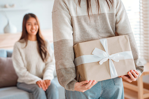 Surprise woman is giving her young girl friend a present at home, New year gift.