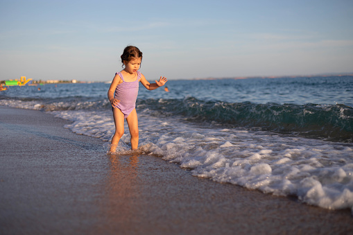 The child is walking carefully on the seashore . The toddler is playing on the beach on the sea waves.