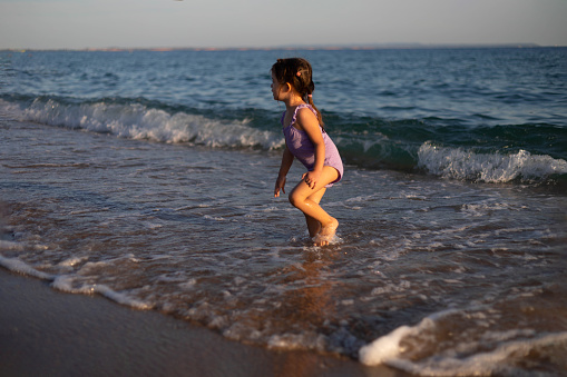 The child is playing with the sea wave. The little girl is standing on the seashore and playing in the sea.