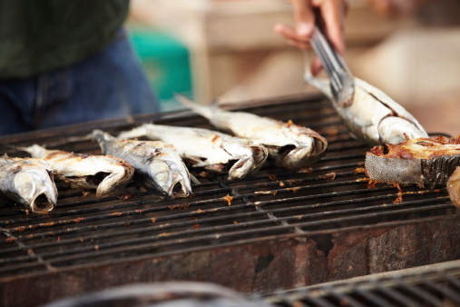 Cropped image of a Thai fish stall owner turning his fish on the grill