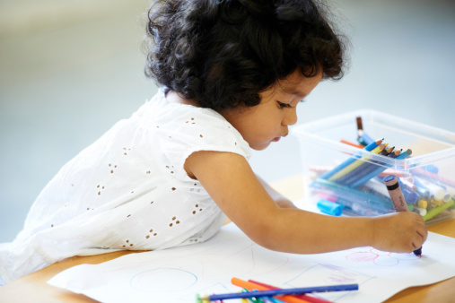 A cute little girl drawing a picture with crayons in preschool class