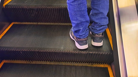 People is going up by escalator in any building with flare or light from the side and shadow on steps in the morning or afternoon.