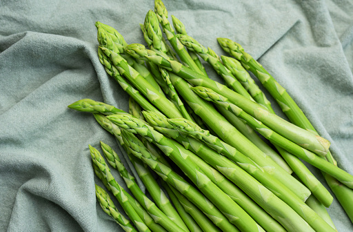 Fresh green asparagus on green textile background. Flat lay