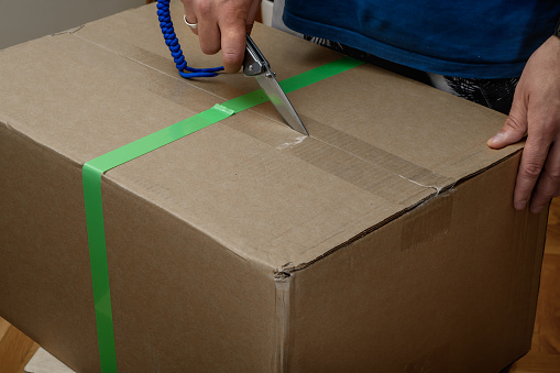 Unpack the courier parcel packed in a cardboard box sealed with tape closeup