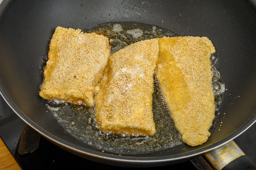 Fish fried in a pan, breaded pieces of fish in hot fat closeup